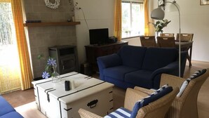 A living room with a blue sofa, wicker chairs, a white chest of drawers, a television, and a fireplace.