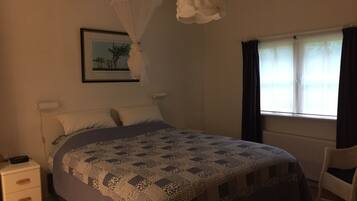 A bedroom with a bed, a bedside table, a chair, a window with curtains, a hanging light fixture, and a wall-mounted picture.