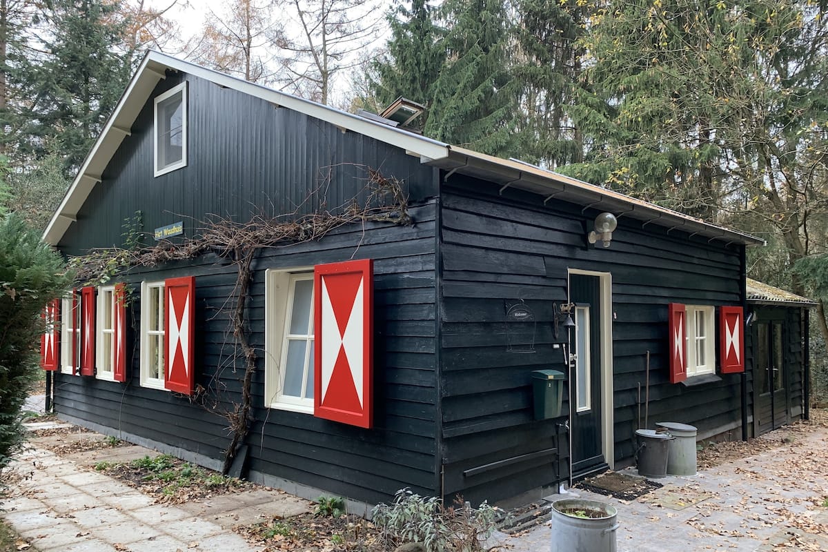 Una cabaña de madera negra con contraventanas rojas, un letrero de bienvenida y un pequeño porche.