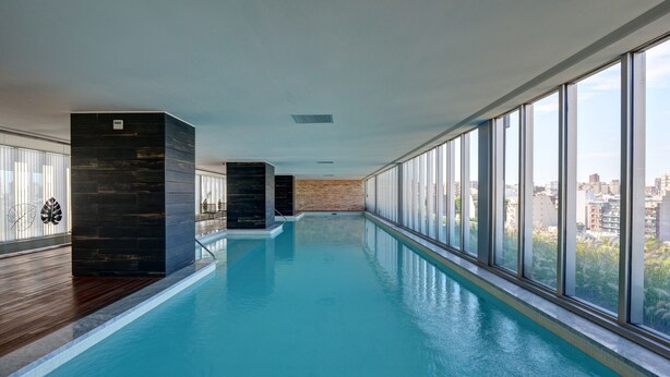 A long indoor swimming pool with a city view, wooden flooring, and dark stone pillars. - Nido x Quartier Dorrego (Buenos Aires)
