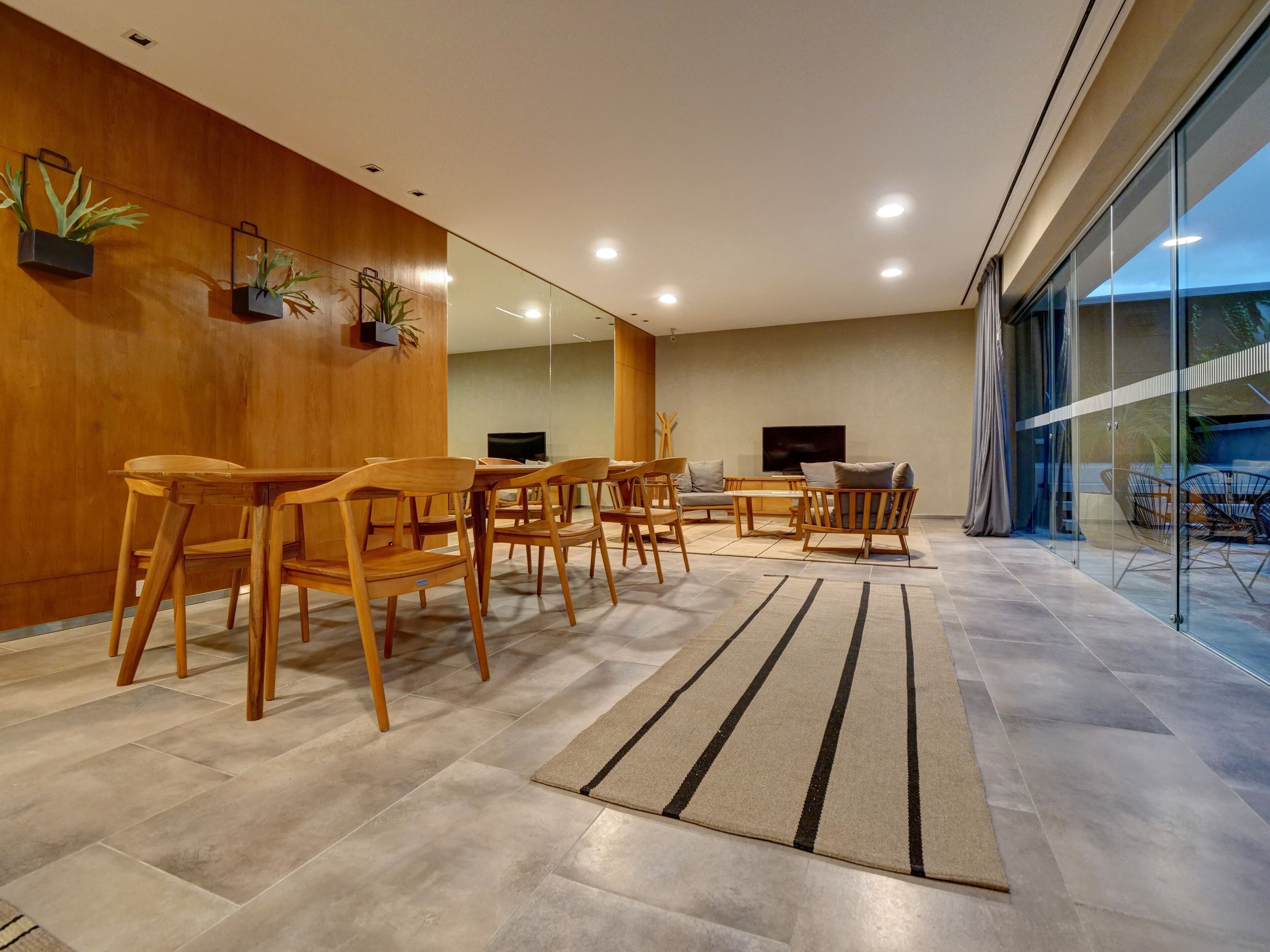 A modern living room with wooden furniture, a flat-screen TV, and a glass wall overlooking a balcony.