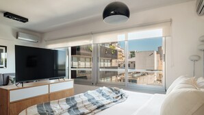 A modern bedroom with a large bed, a flat-screen TV on a wooden dresser, and a view of the city through large windows. - Nido x Quartier Dorrego (Buenos Aires)