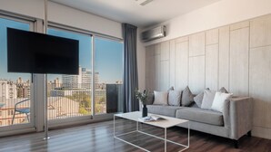 A modern living room with a grey sofa, a white coffee table, and a large window offering a city view. - Nido x Quartier Dorrego (Buenos Aires)