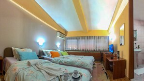 A hotel room with two beds, a desk with a computer, a bedside table with books, and a bathroom with a sink and mirror. - Hotel Square (Skopje)