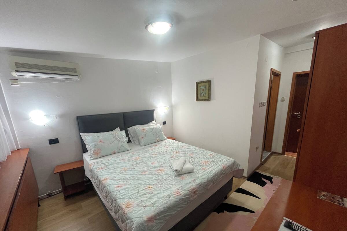 Quarto com uma cama, mesas de cabeceira, ar condicionado e uma porta.