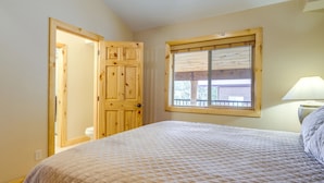 A bedroom with a bed, a wooden door, a window, and a nightstand with a lamp.