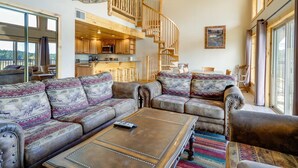 A spacious living room with a large sofa set, a coffee table, and a staircase leading to an upper level.