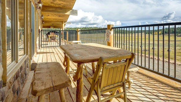 A wooden deck with a table and chairs, overlooking a fenced area with a view of trees and a clear sky.