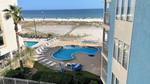 Une piscine avec des chaises longues, une plage en arrière-plan et un bâtiment doté de grandes fenêtres.