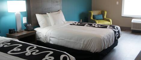 A hotel room with a bed, bedside table, lamp, chair, and window.