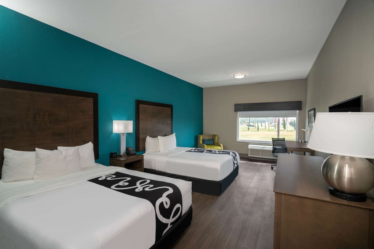 Habitación de hotel con dos camas, un escritorio, una silla y un televisor.