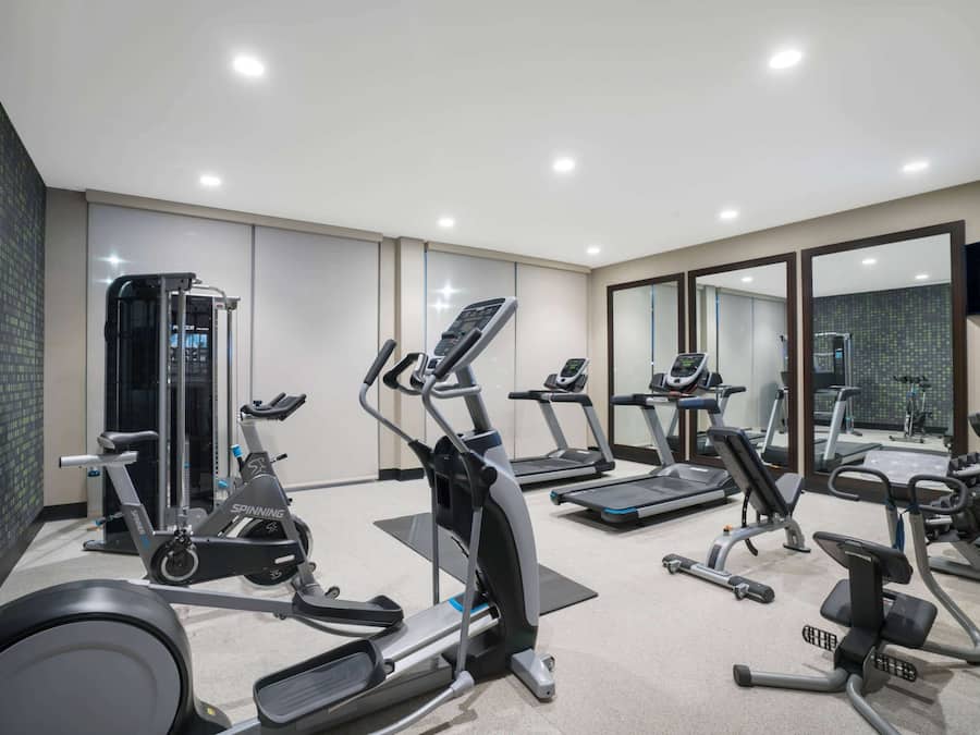 A gym with various exercise machines, including treadmills and elliptical trainers, and a large mirror on the wall.
