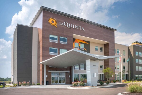 Un hotel moderno con un llamativo letrero de 'LaQuinta', un acceso cubierto y un área ajardinada con flores.