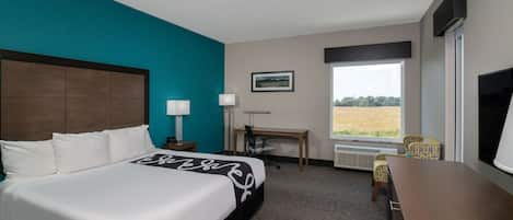 Ein Hotelzimmer mit einem großen Bett, einem Schreibtisch, einem Sessel, einem Fernseher und einem Fenster mit Blick ins Freie.