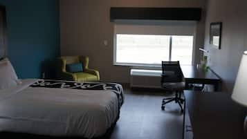 A hotel room with a bed, a desk, a chair, a window, and a radiator.