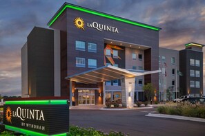 Un hotel moderno con una entrada destacada, un cartel que indica que es La Quinta by Wyndham, y una vista despejada del estacionamiento.