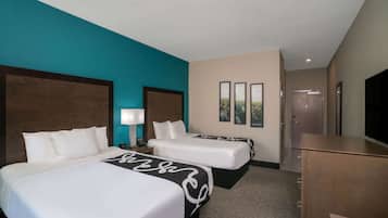 A hotel room with two beds, a desk, a TV, and a door leading to a bathroom.