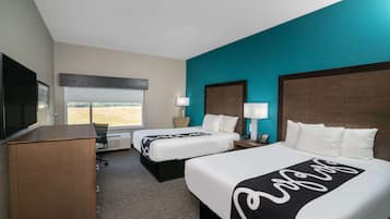 Quarto de hotel com duas camas, uma escrivaninha, uma televisão e uma janela com vista.