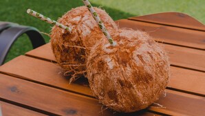 Dois coco com canudos sobre uma mesa de madeira perto de uma piscina.