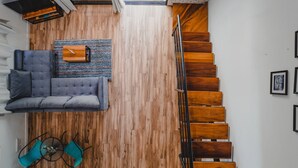 Um interior moderno com piso de madeira, um sofá cinza, uma mesa pequena com cadeiras e uma escada com degraus de madeira.