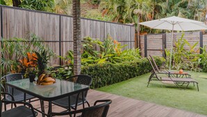 Um pátio com mesa e cadeiras de vidro, cercado por vegetação exuberante e um cercado de madeira.