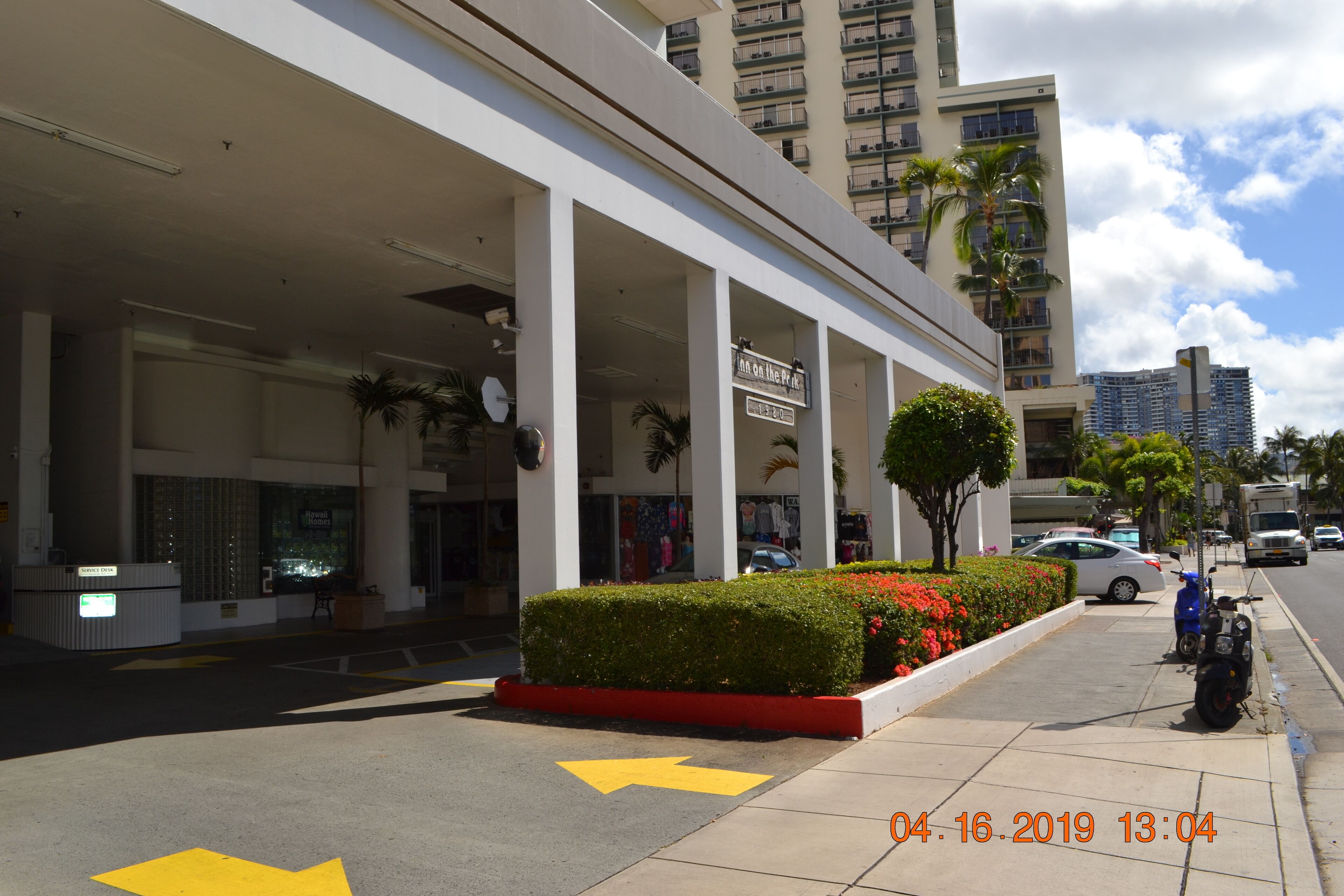 A hotel with a modern facade, a reception desk, and a parking area with cars and a motorcycle.