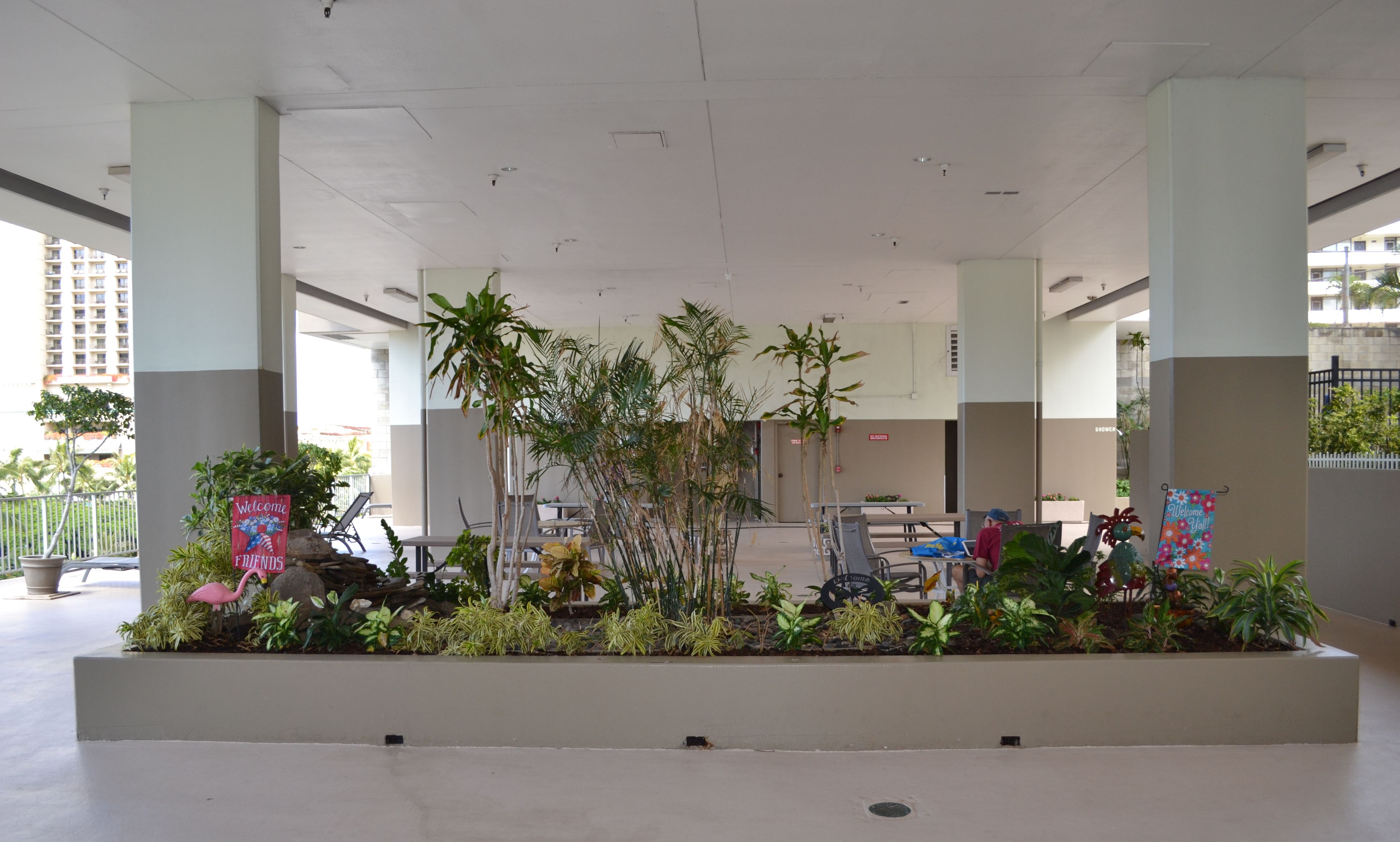 Amplio espacio interior con un macetero central con diversas plantas, un letrero de bienvenida y algunas sillas.