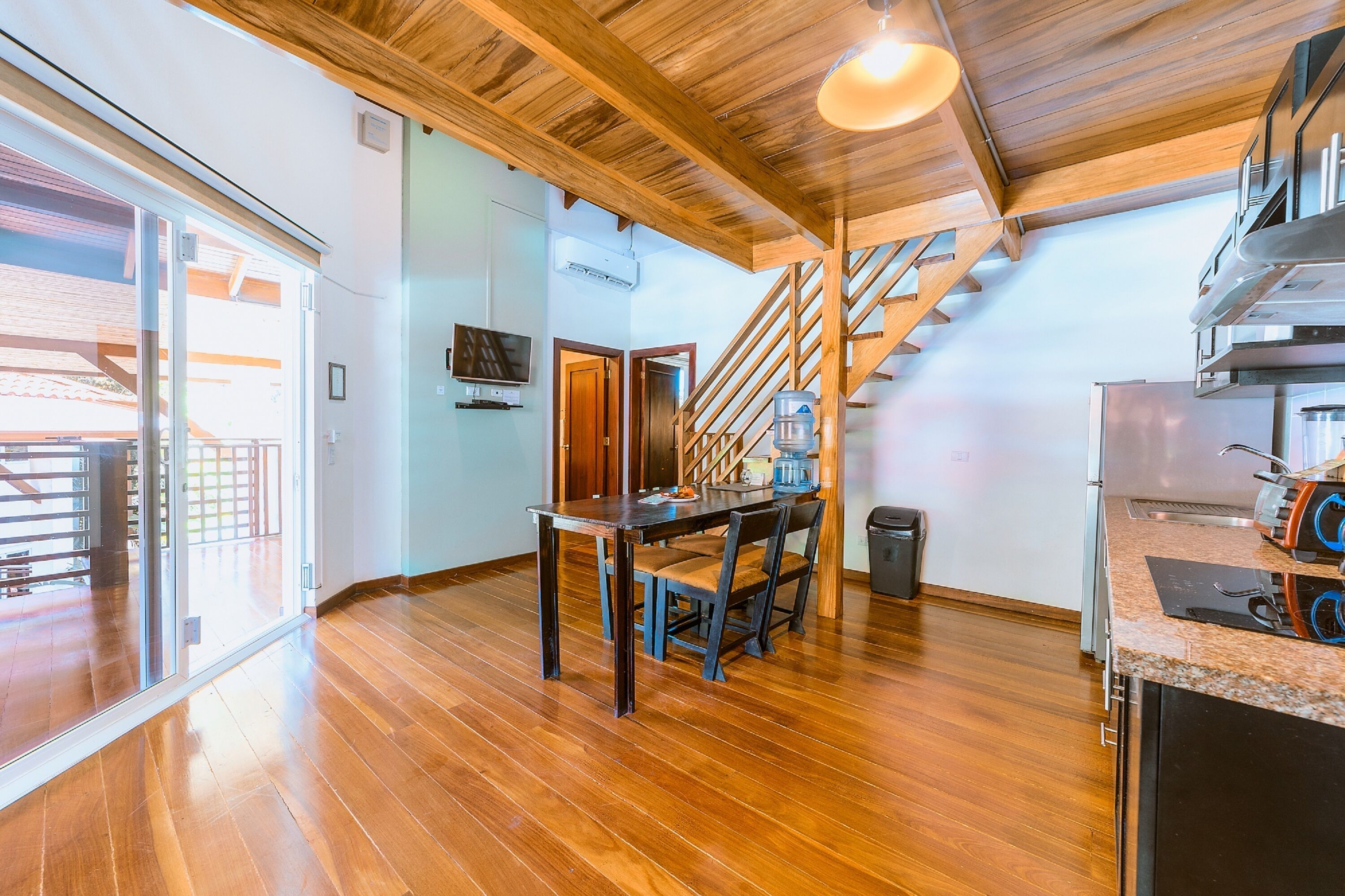 A spacious kitchen with wooden flooring, a dining area with a table and chairs, a staircase, and a large window.