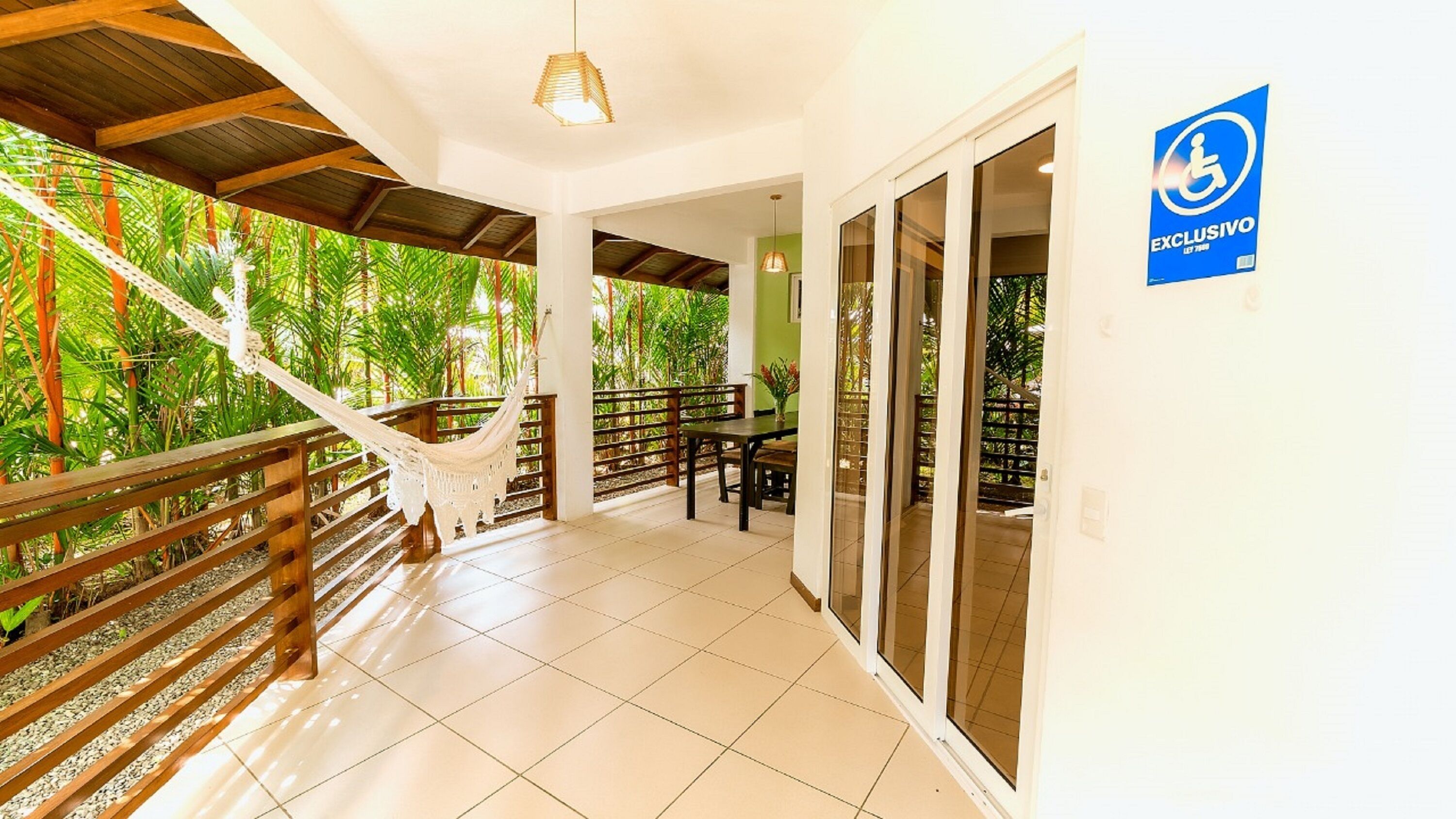 A covered outdoor area with a hammock, wooden railing, and a view of lush greenery.