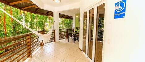 A covered outdoor area with a hammock, wooden railing, and a view of lush greenery.