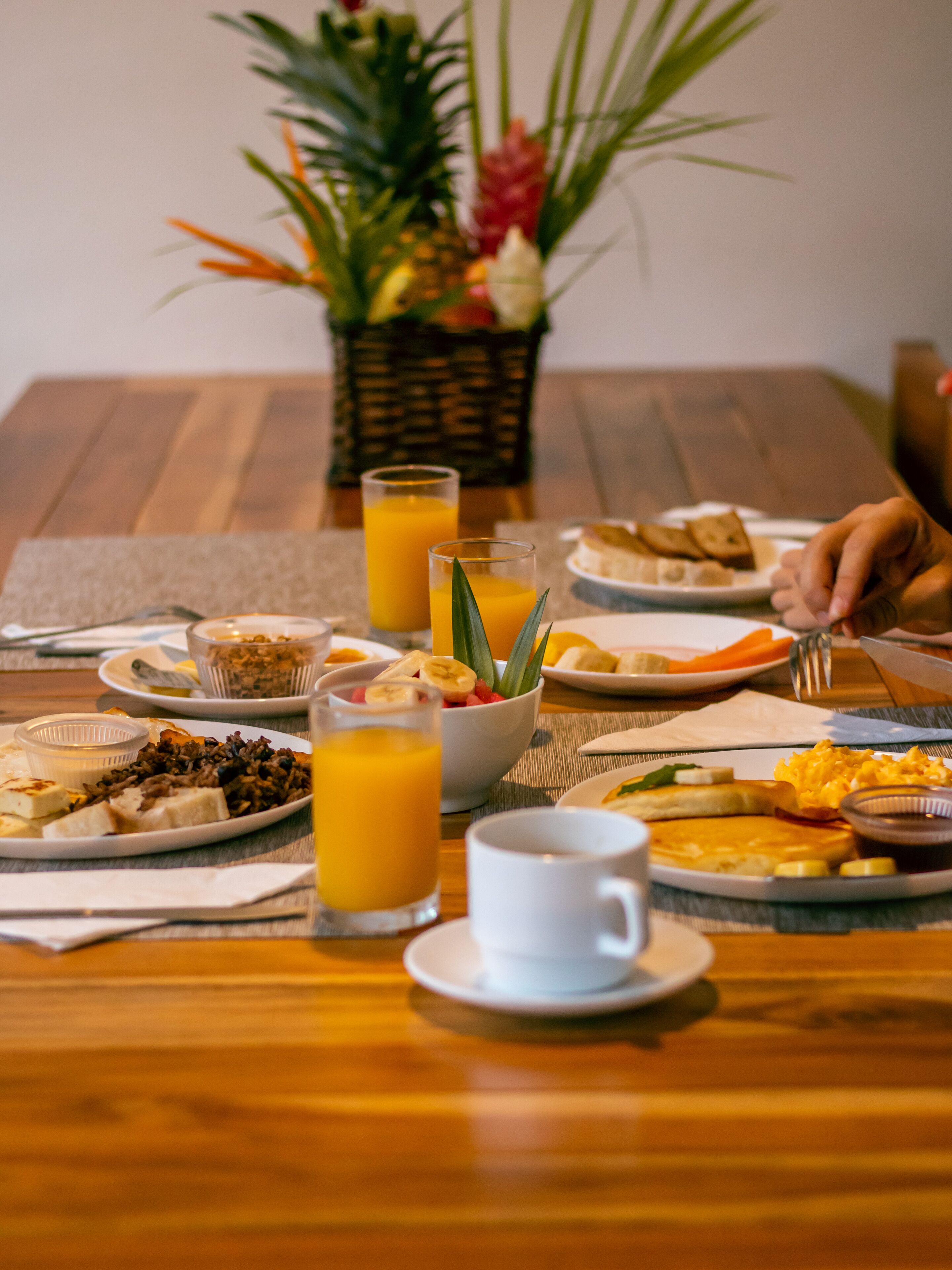 A breakfast table with various dishes, including toast, eggs, and fruit. There are glasses of orange juice and a white cup.