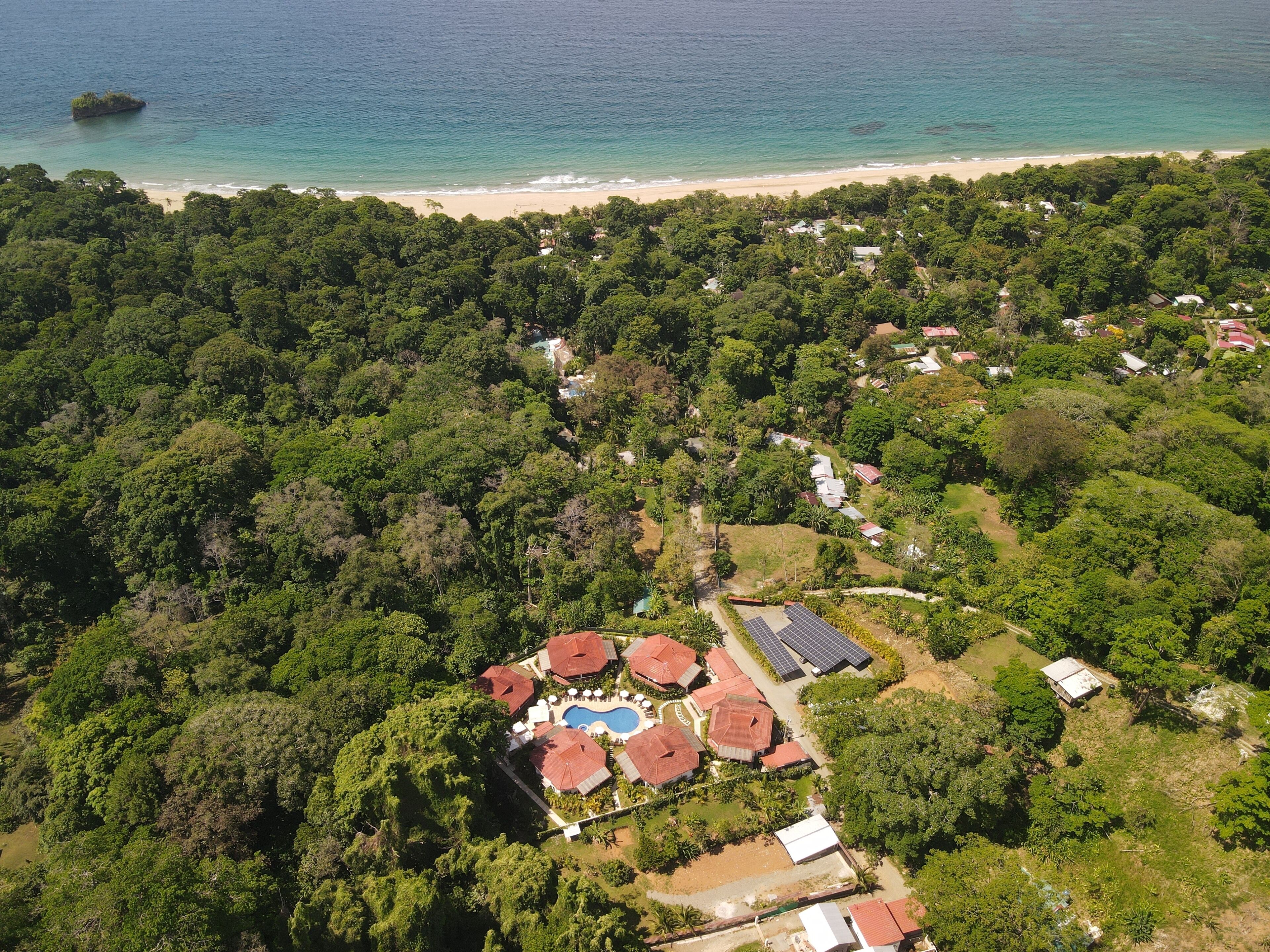 An aerial view of a resort with a pool area, solar panels, and a beach.