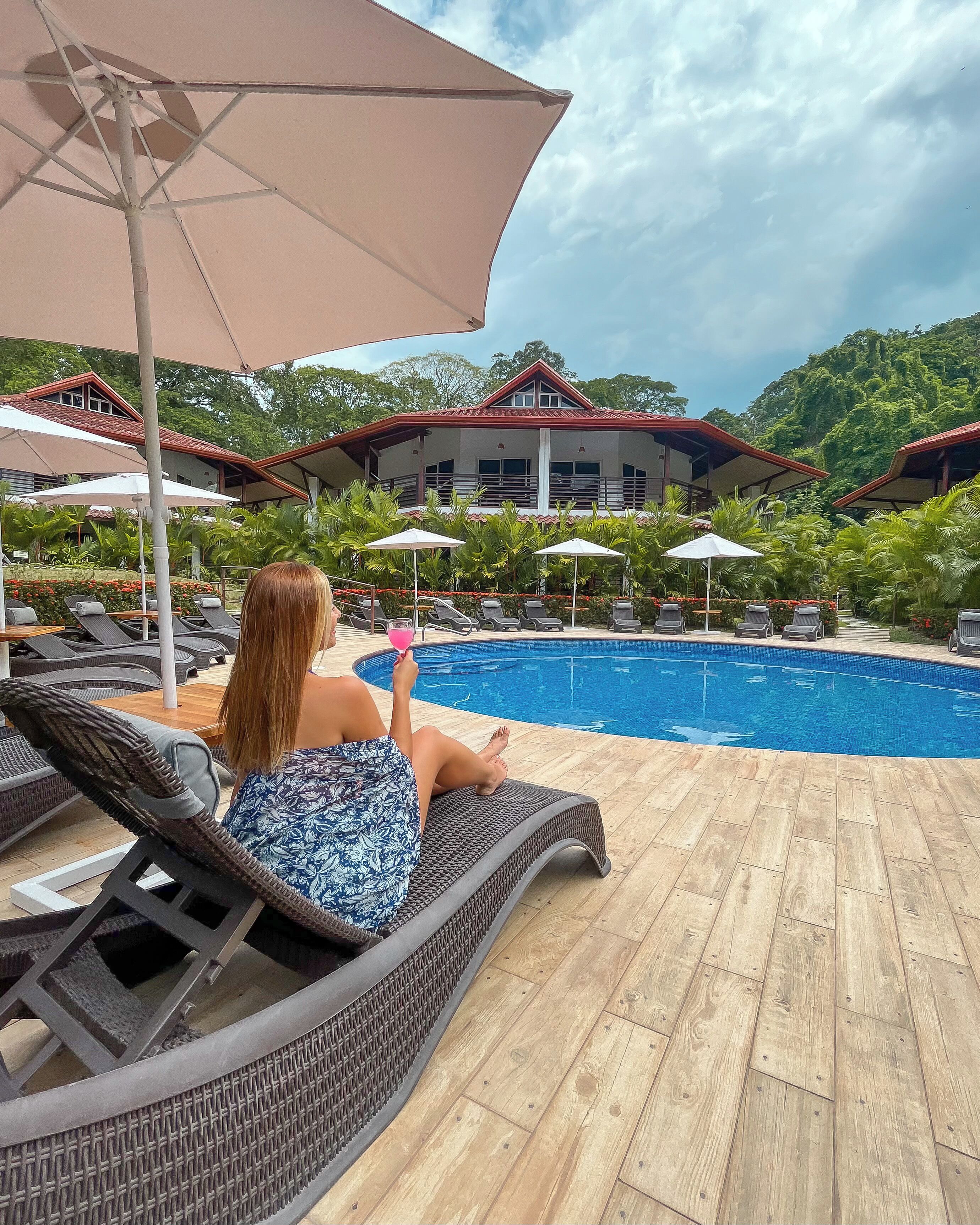 A poolside area with lounge chairs, umbrellas, and a view of a building with a red roof.