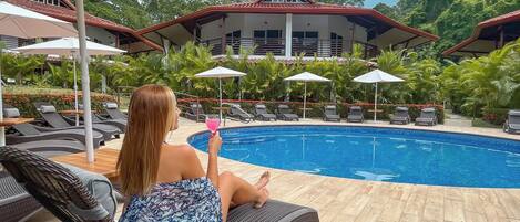 A poolside area with lounge chairs, umbrellas, and a view of a building with a red roof.