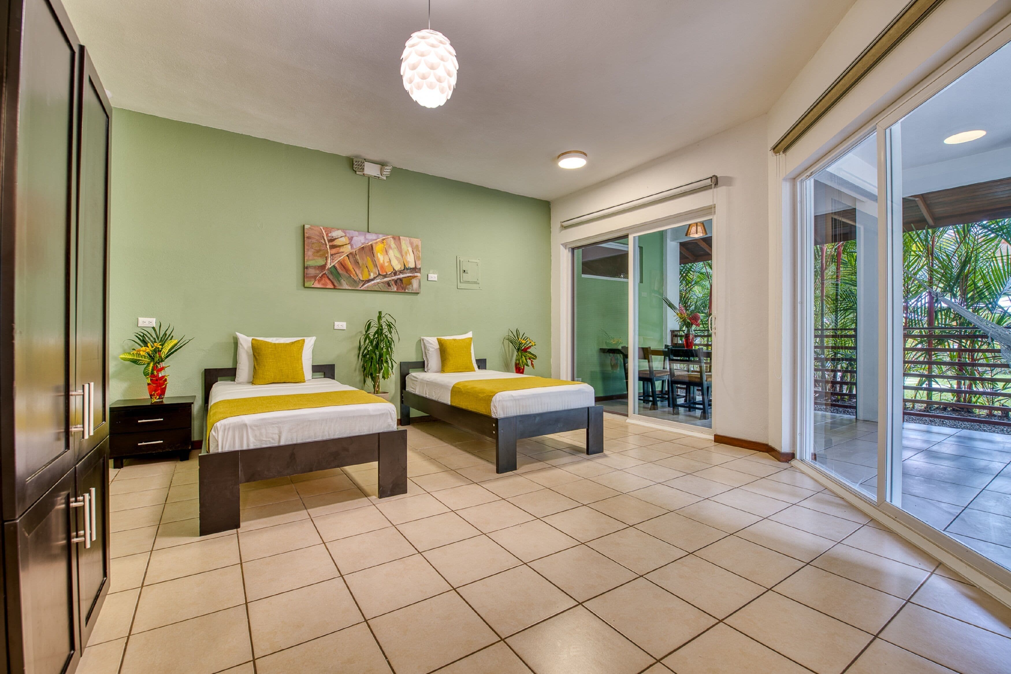 Une chambre d’hôtel moderne avec deux lits, une grande fenêtre et un coin repas visible à travers les portes vitrées.