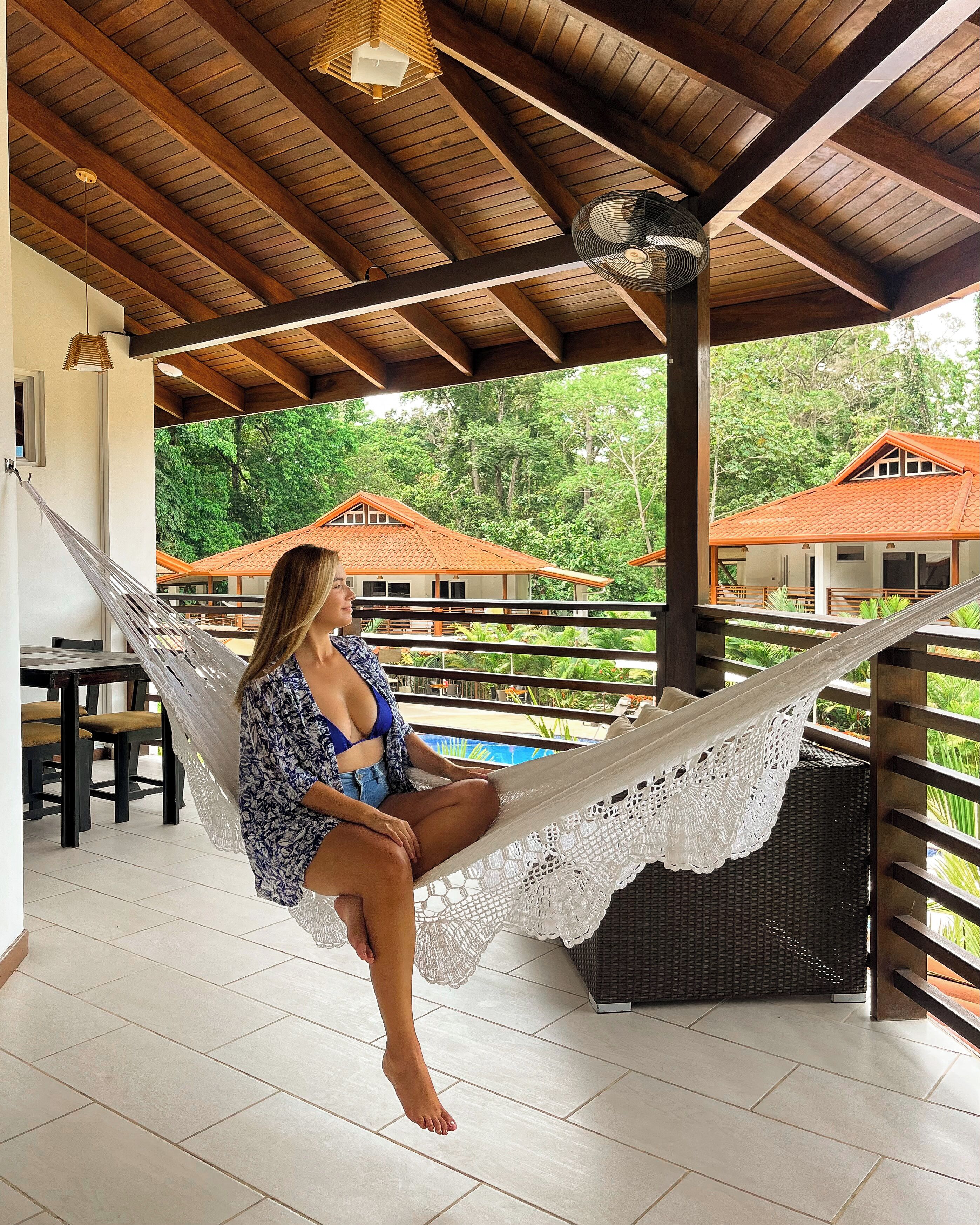 A hammock under a wooden ceiling with a view of a house and greenery.