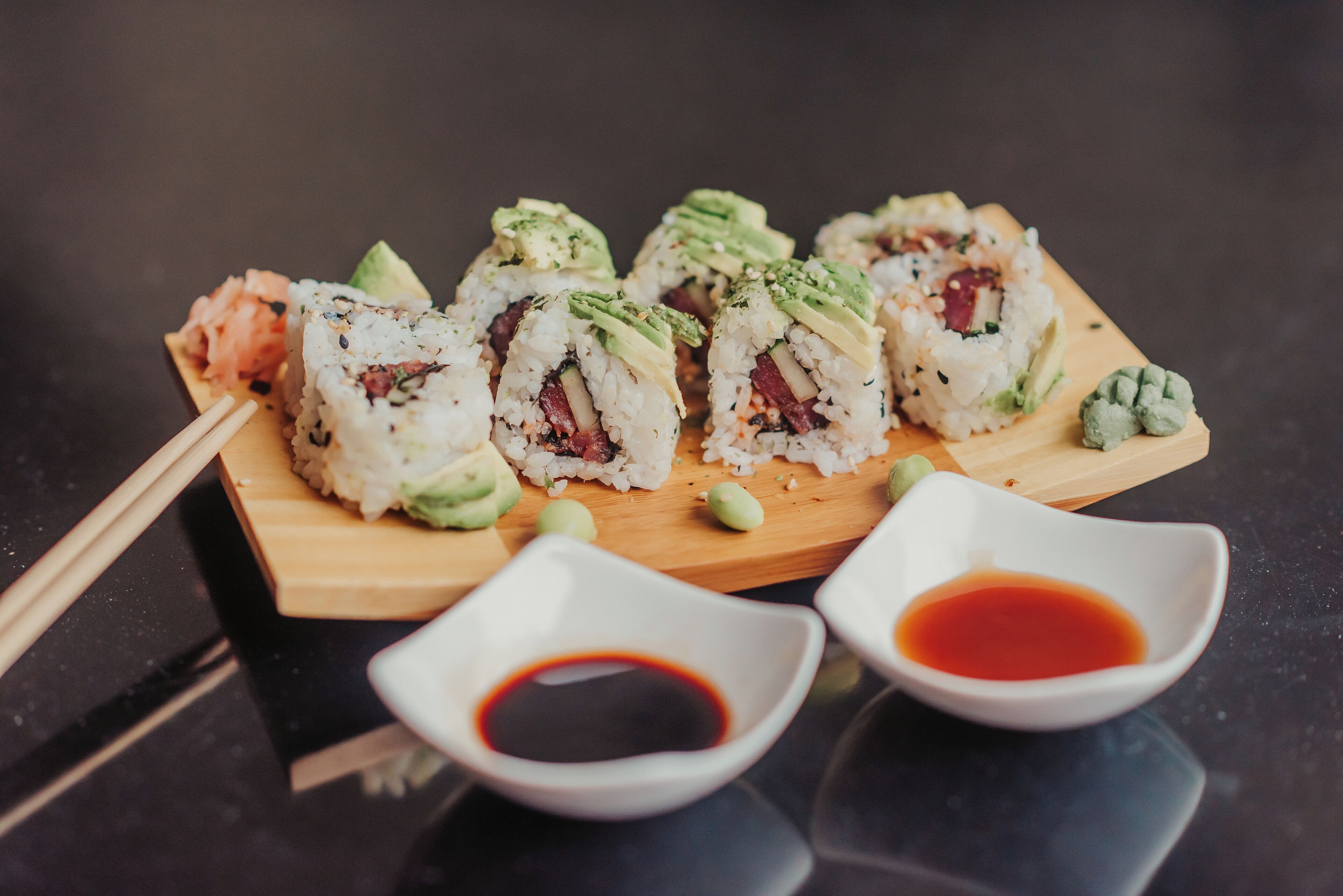 Sushi on a wooden board with two small bowls of soy sauce.