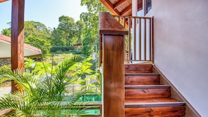 A wooden staircase leading to a covered outdoor area with lush greenery and a view of a house in the background. - Terrazas del Caribe Hotel (Cahuita)