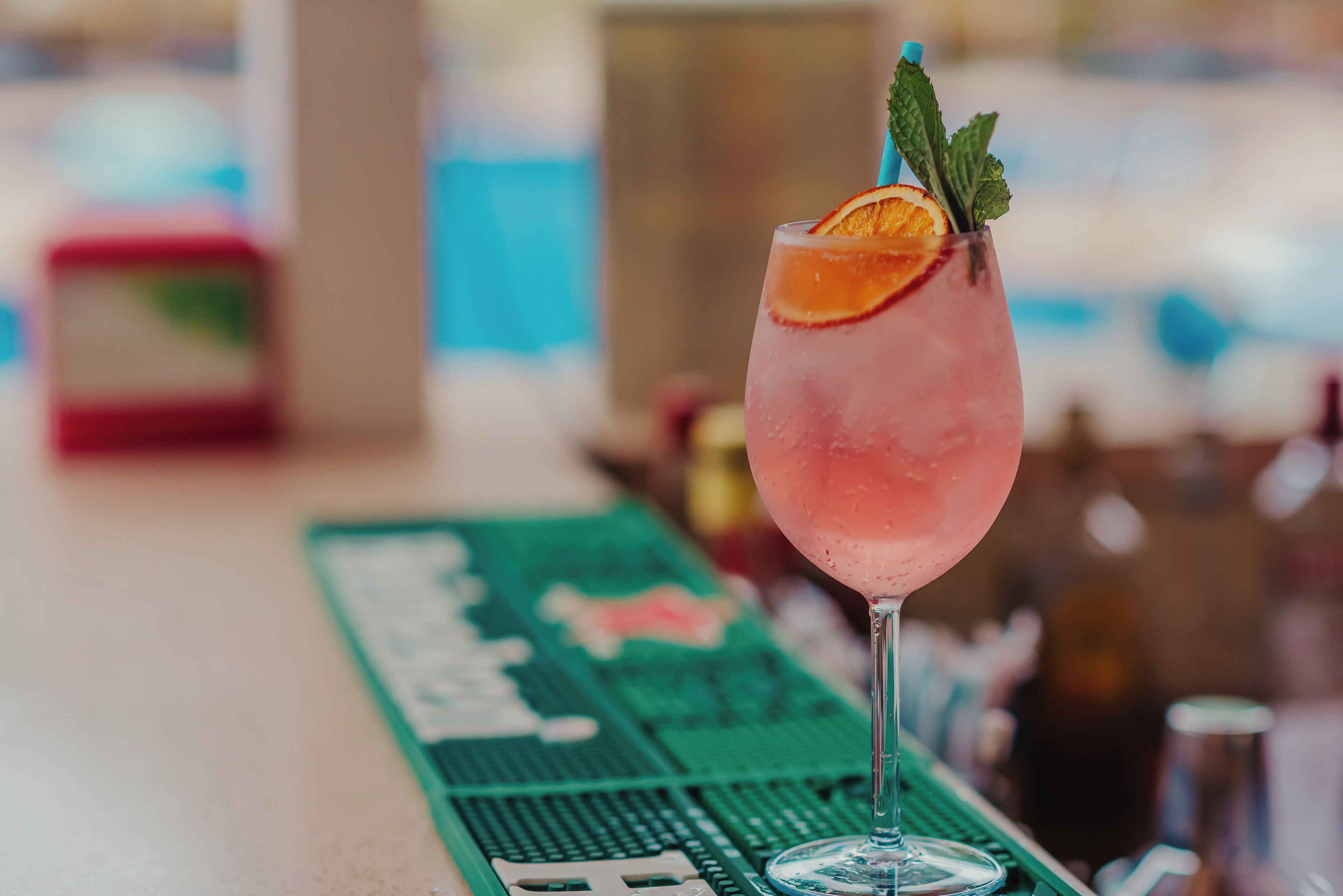 A cocktail glass with a slice of orange and mint on a bar counter.
