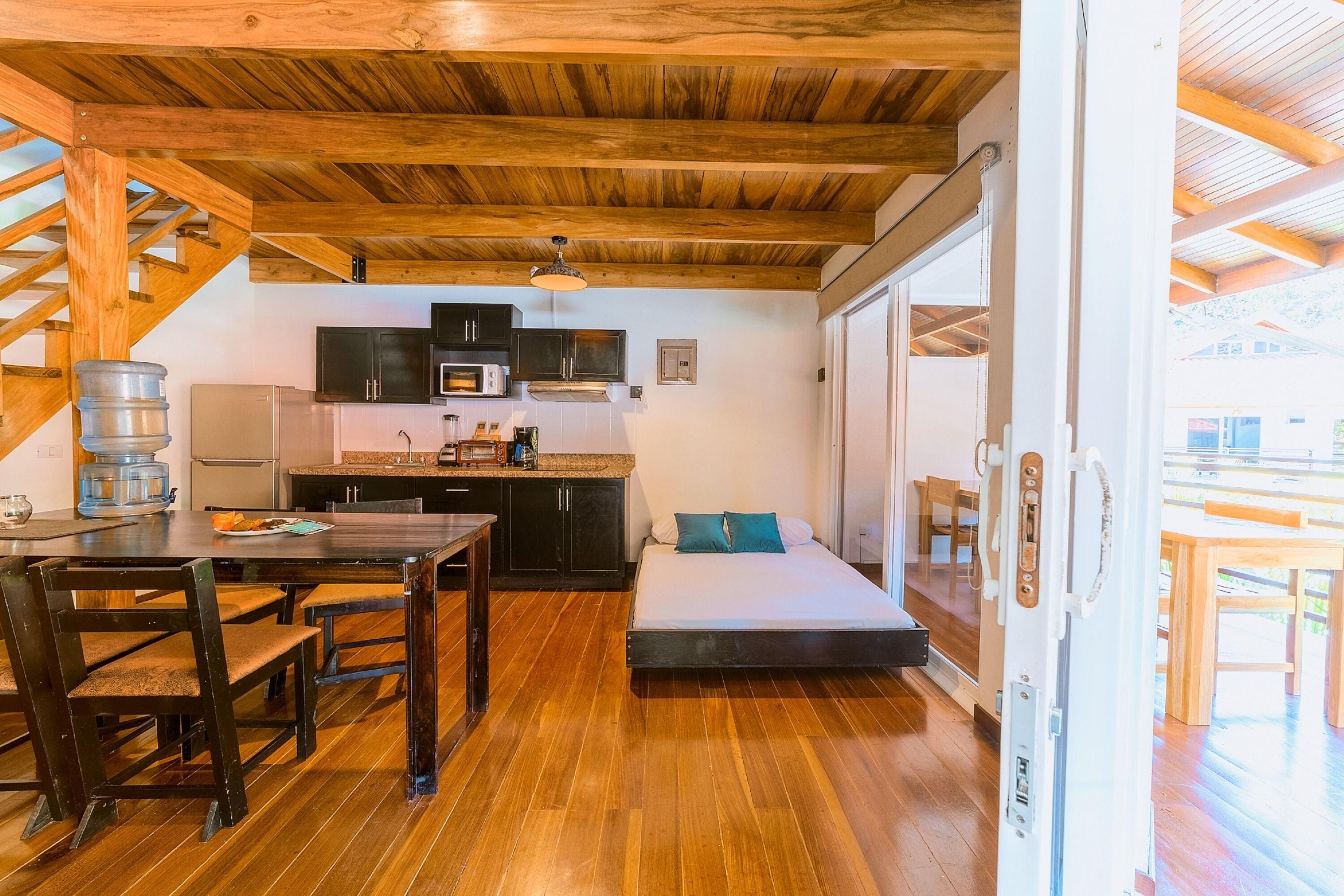 A compact kitchen with modern appliances, a dining area with wooden furniture, and a cozy sleeping area with a sofa and pillows.