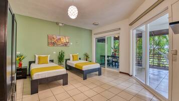 Quarto de hotel com duas camas, área de refeições e porta de vidro corrediça para o exterior.