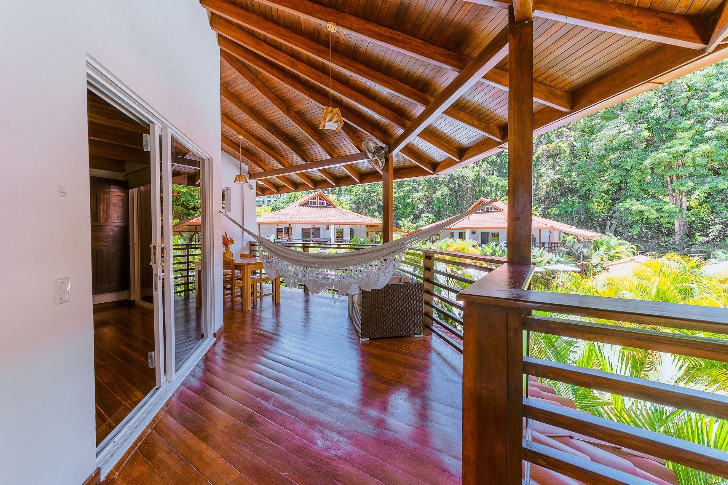 A wooden deck with a hammock, a wicker chair, and a view of a lush garden.