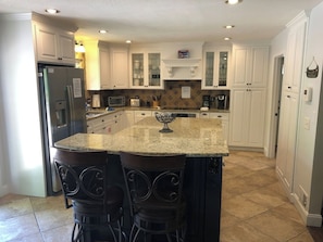 A kitchen with white cabinets, a granite countertop, a refrigerator, a coffee maker, and a microwave.