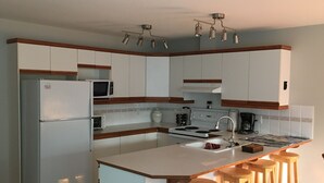 Een moderne keuken met witte kastjes, een ingebouwde magnetron, een fornuis en een spoelbak. Er staan houten krukken bij het eiland.