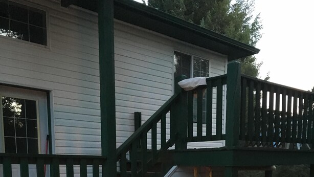Een terras met een vuurkuil, witte kunststof stoelen en een huis met een groen terras en een trap.