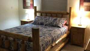 Een slaapkamer met een houten bedframe, een raam met zonwering, een nachtkastje met een lamp en een aan de muur hangend kunstwerk.