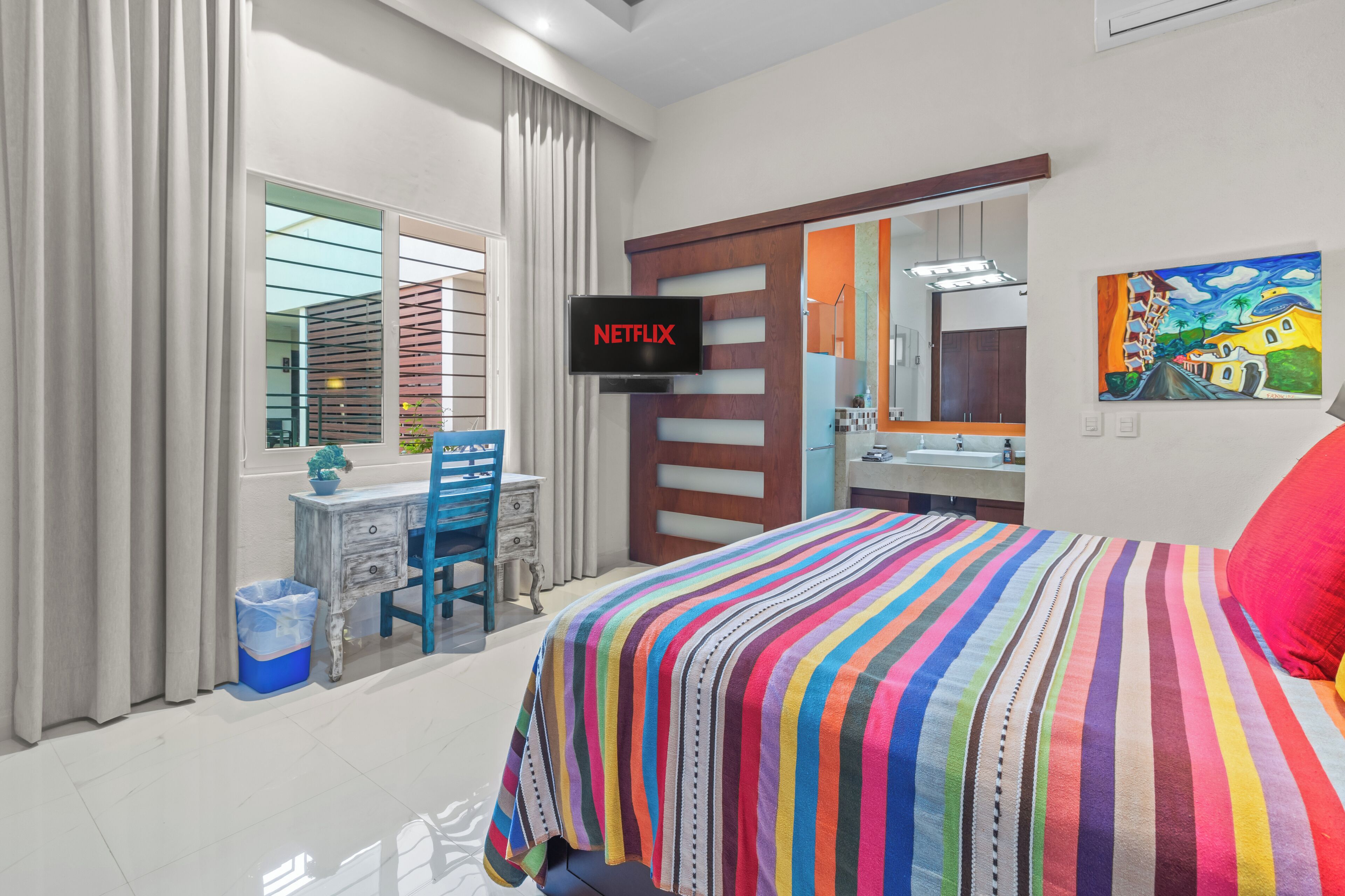 A modern hotel room with a large bed, a desk with a chair, a TV, and a bathroom mirror.
