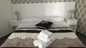 A neatly made bed with a patterned bedspread, two bedside lamps, and a decorative pillow. - Alambrado Rooms & Suites (Naples)
