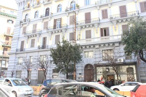 A multi-story building with balconies, storefronts, and parked cars. - Alambrado Rooms & Suites (Naples)