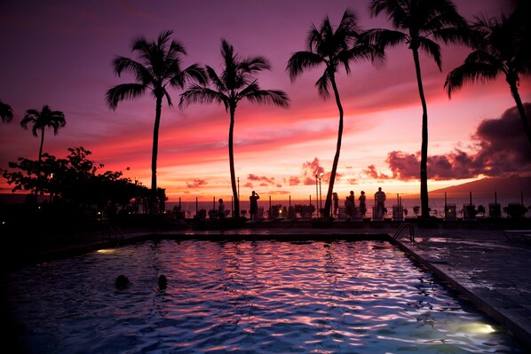 A sunset view with palm trees and a pool area.